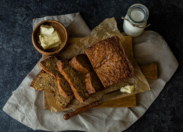Banana bread with butter and milk on a chopping board