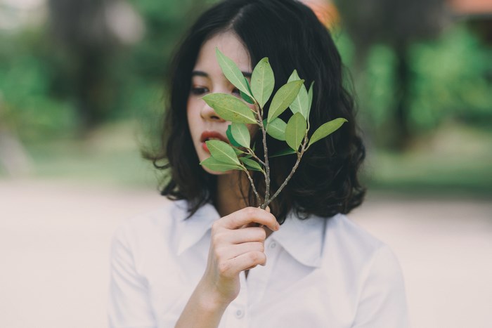 Woman holding a green branch in front of her face