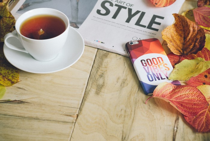 Cup of tea, iPhone, and autumn leaves on a wooden table