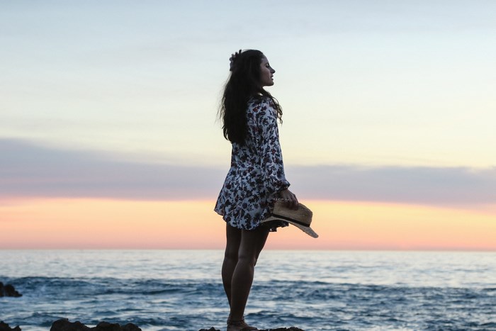 Woman holding a hat at sunset by the ocean
