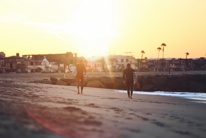 Two surfers walk on the beach at sunset