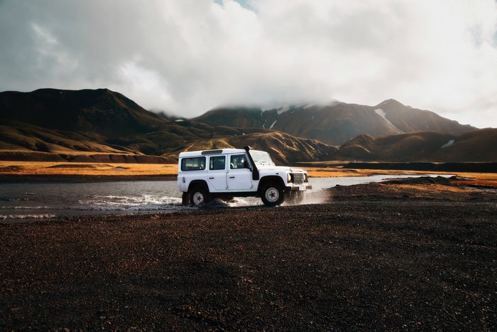 White Land Rover Defender driving through water in mountains