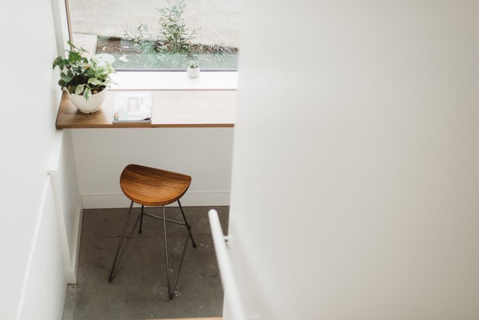 Minimalist workspace with wooden stool and plant by window