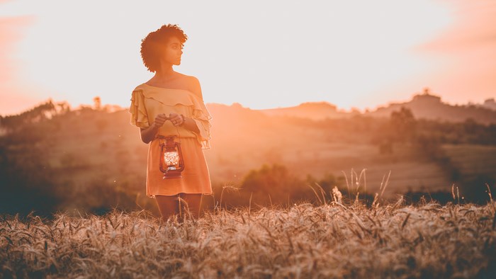Woman holding a lantern in a field at sunset