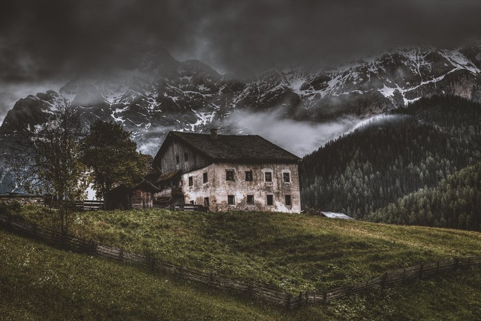 Old house on a grassy hill with mountains