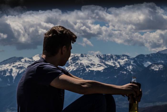 Man with beer looking at snow-capped mountains