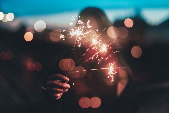 Person holding sparklers with bokeh lights
