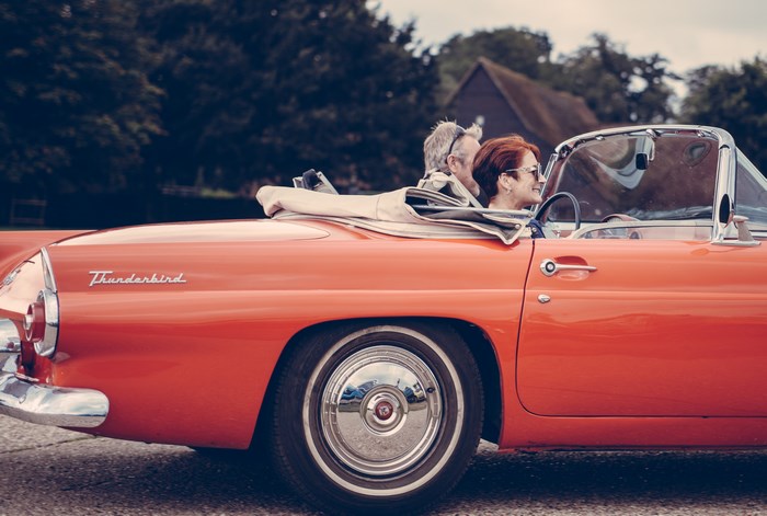 Couple driving a red Ford Thunderbird convertible