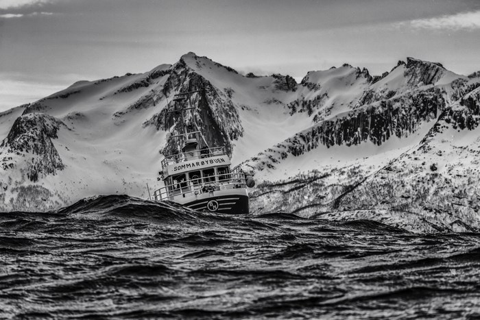 Fishing boat on a rough sea with snow-capped mountains
