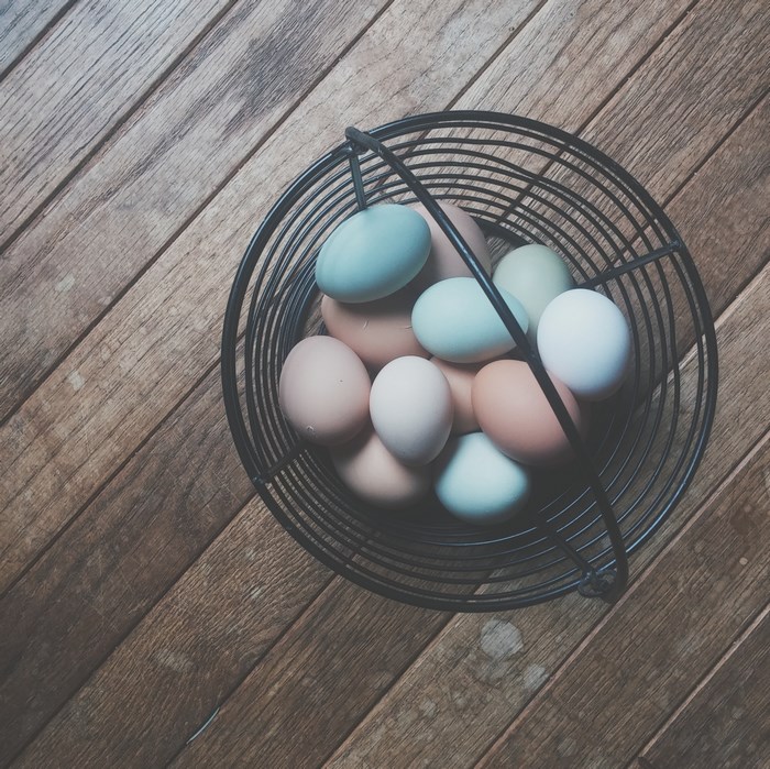 Basket of Multicolored Farm Fresh Eggs on Wooden Floor