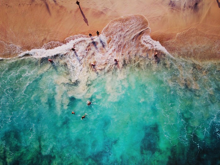 People swimming and walking on a sandy beach by the ocean