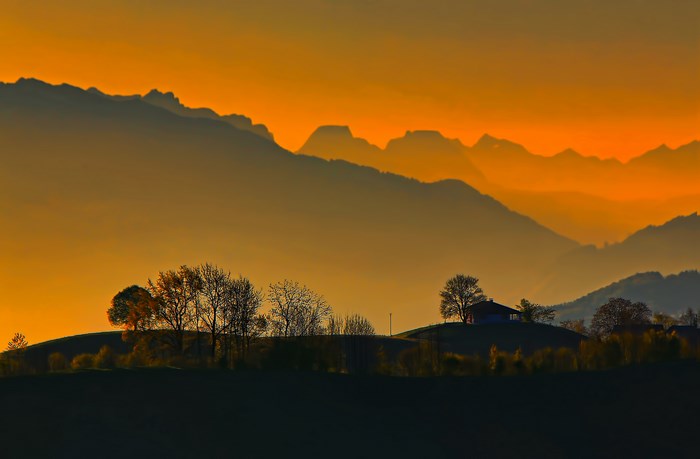 Silhouetted mountains at sunset with trees and a house