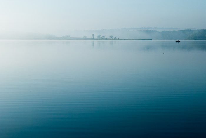 A lone fisherman in a boat on a misty lake at dawn