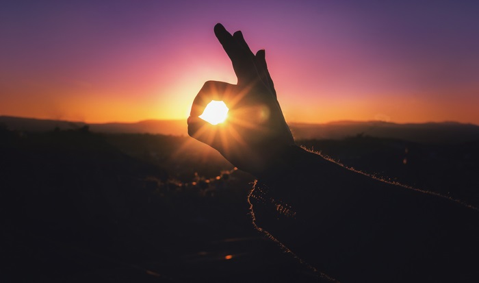 Silhouette of a hand making an OK sign at sunset