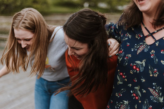 Three women laughing and hugging outdoors