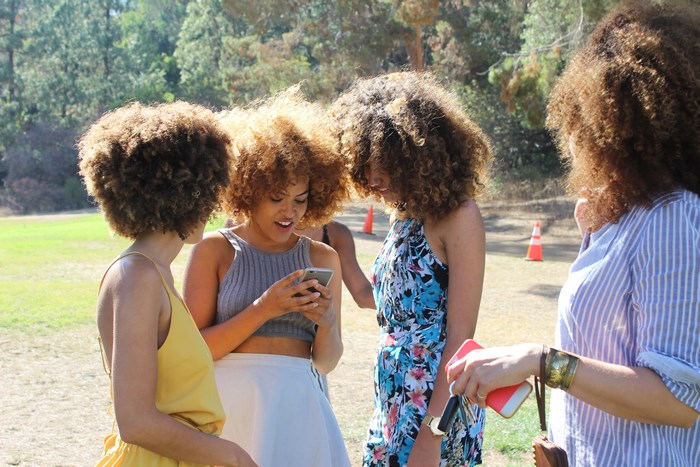 Four women with curly hair looking at a phone