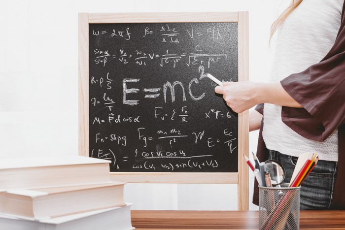Woman teaching physics formulas on a chalkboard