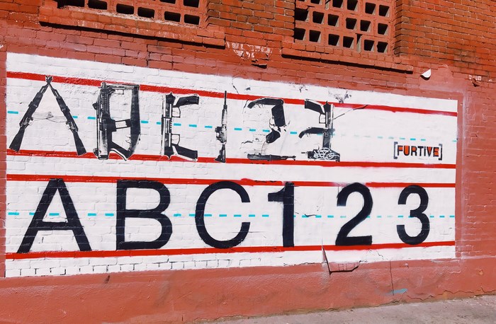 Graffiti art of guns forming letters and numbers on a brick wall