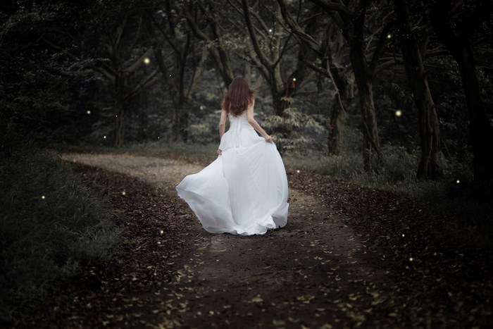 Woman in white dress running in a dark forest