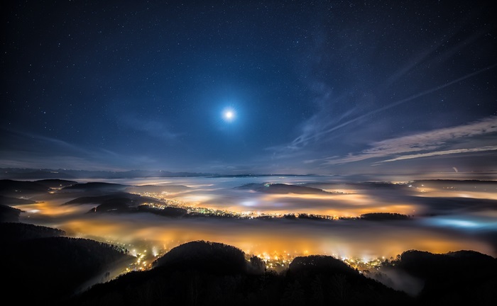 Night sky over a foggy valley with city lights