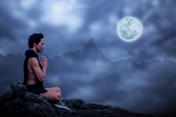 Man meditating on a rock under the moon