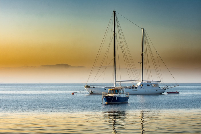 Two yachts and a small boat on the water at sunset
