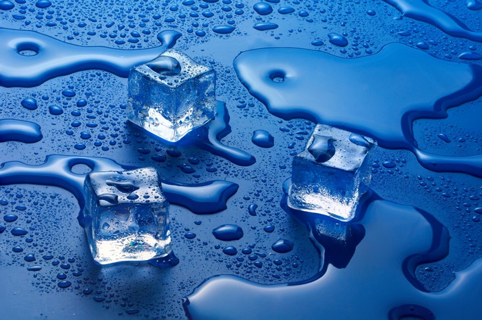 Ice cubes melting on a blue surface with water droplets