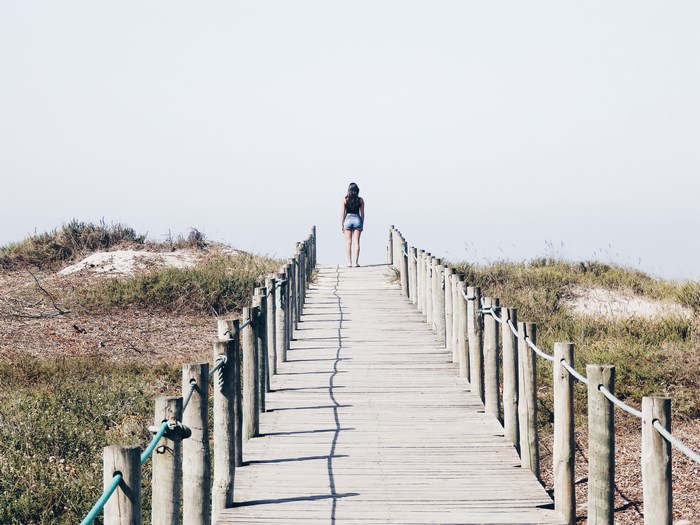Woman walking on a wooden path by the beach