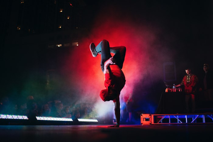 Breakdancer performs a handstand on stage with red lighting