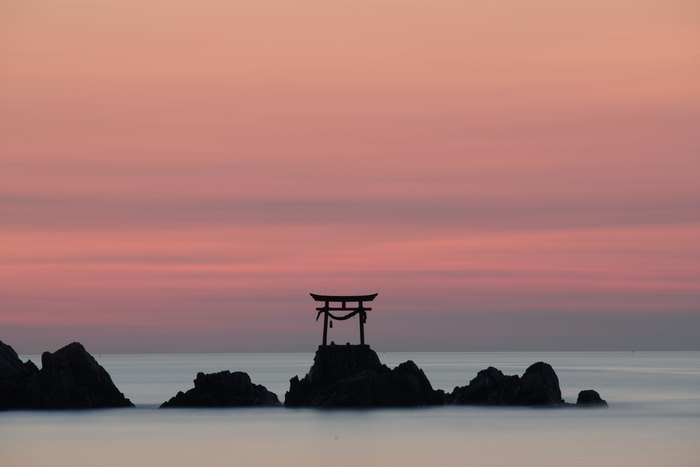Torii gate on rocks at sunrise over the ocean