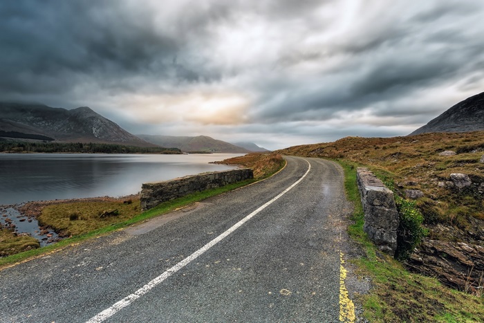 Road by a lake with mountains under cloudy sky 4K