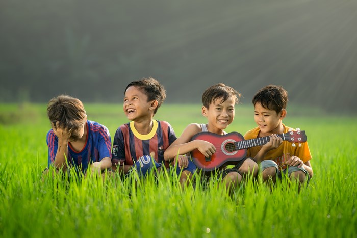 Four boys playing guitar in a grassy field