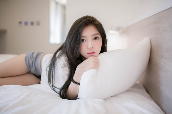 Asian woman lying on a bed with a pillow