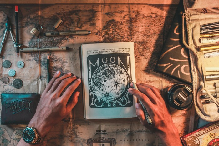 Hands drawing a moon on a map with art supplies