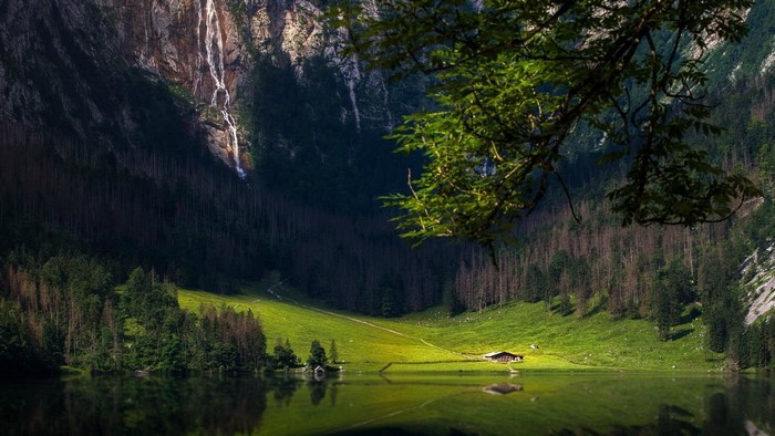 Waterfall cascading down a rocky mountain into a lake with a house