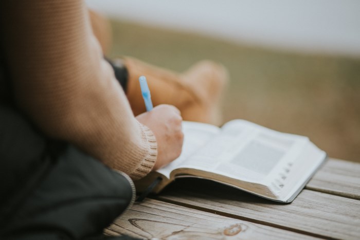 Person writing in a bible with a pen