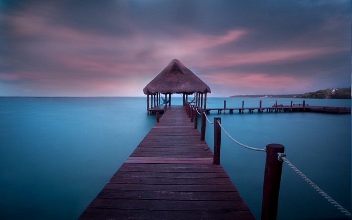Tropical dock with thatched hut over turquoise water at sunrise