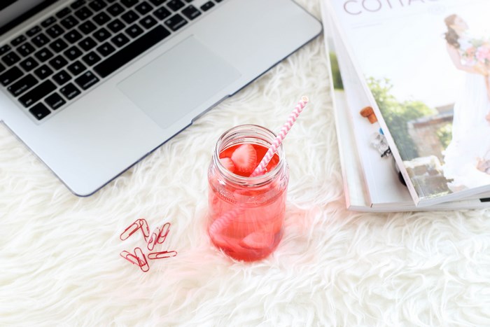 MacBook, strawberry drink, and magazines on a fluffy rug