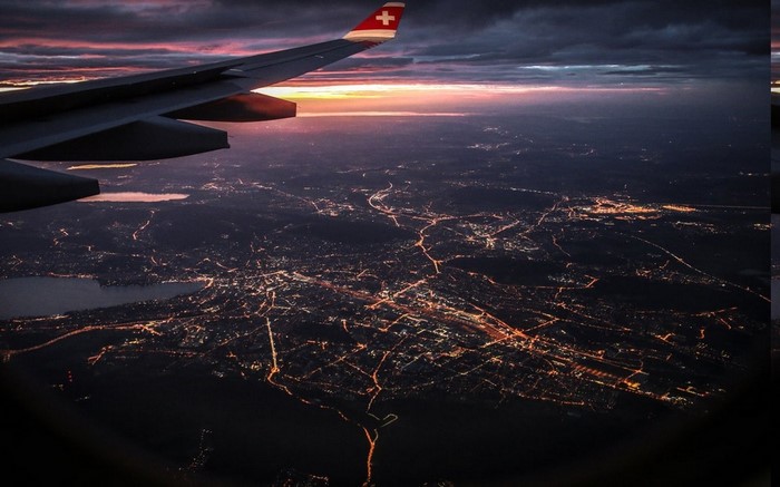 Airplane wing over city lights at sunset