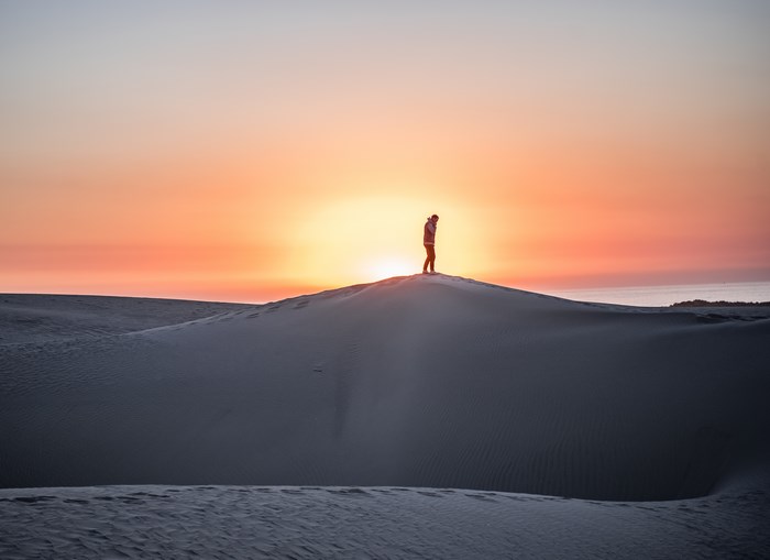 Man standing on sand dune at sunrise