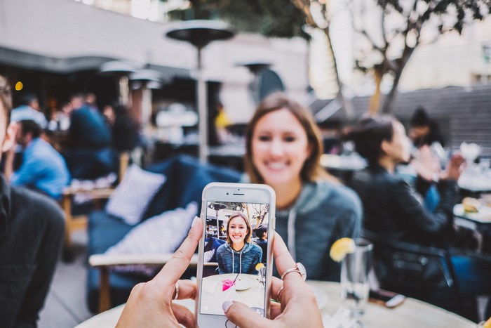 Woman taking a photo of her friend at an outdoor cafe