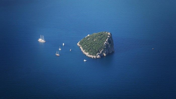 Island with boats in blue sea, aerial view