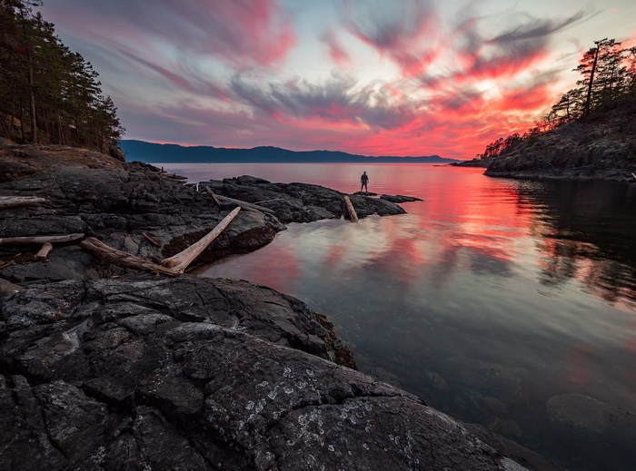 Person standing on rocks at sunset by the ocean