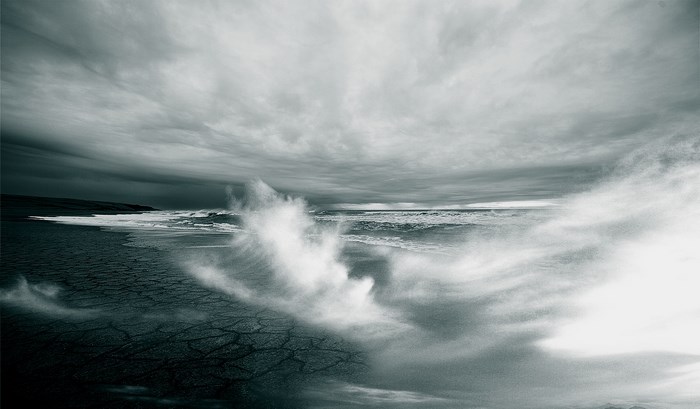 Monochrome ocean waves crashing on a cracked shore under stormy clouds