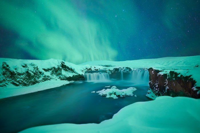 Northern Lights over a snowy waterfall at night