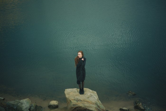 Woman with red hair standing on a rock by the water