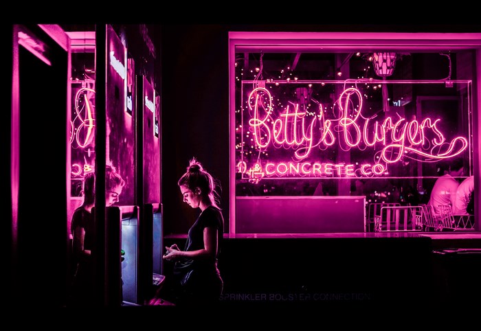 Betty's Burgers neon sign with woman at ATM