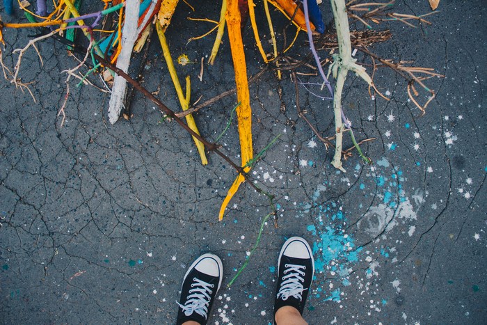 Person wearing black Converse sneakers standing on cracked asphalt with colorful sticks