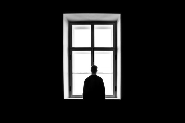 Silhouette of Person Standing Alone by Window in Darkness
