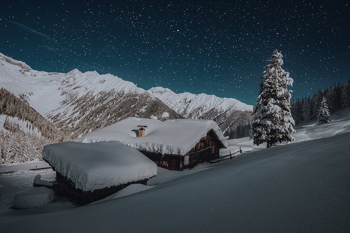 Snowy cabin in mountains under starry night sky